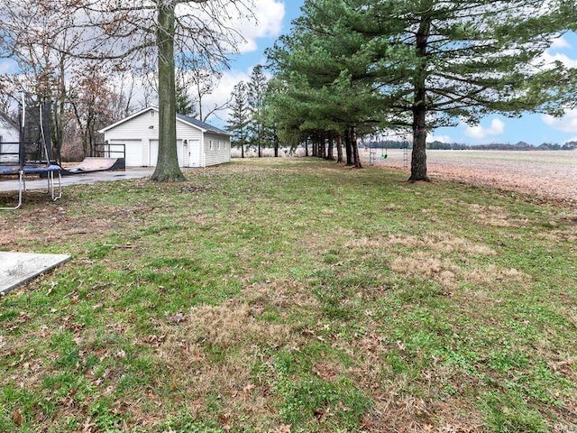 view of yard with an outbuilding, a trampoline, a garage, and a rural view