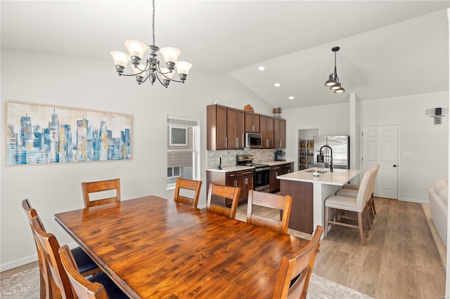 dining area featuring a notable chandelier, light hardwood / wood-style floors, sink, and vaulted ceiling