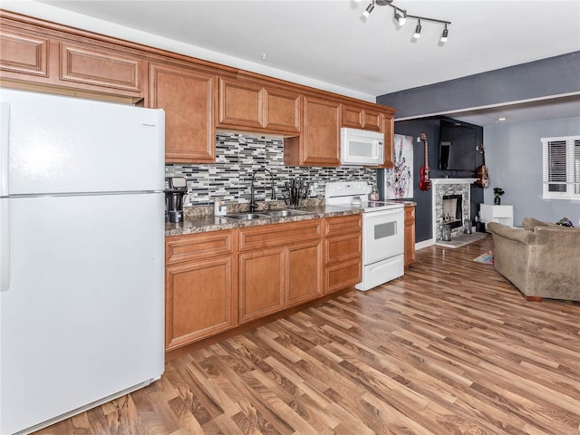 kitchen with tasteful backsplash, white appliances, sink, light hardwood / wood-style floors, and a stone fireplace