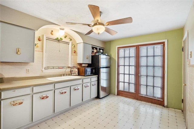 kitchen with backsplash, ceiling fan, sink, and stainless steel refrigerator