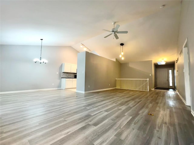 unfurnished living room featuring ceiling fan with notable chandelier, light wood-type flooring, and vaulted ceiling