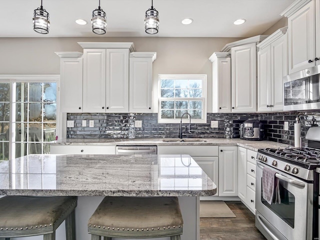 kitchen featuring appliances with stainless steel finishes, light stone counters, a breakfast bar, white cabinets, and hanging light fixtures