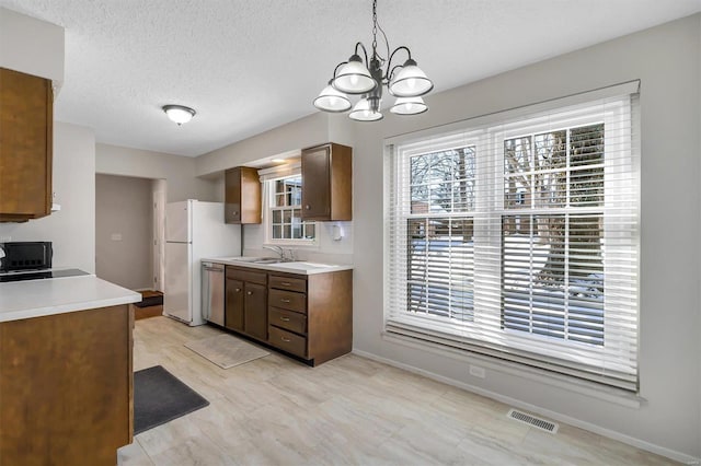 kitchen featuring stainless steel dishwasher, a textured ceiling, a chandelier, hanging light fixtures, and sink