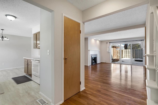 hall with a textured ceiling, light hardwood / wood-style flooring, and an inviting chandelier