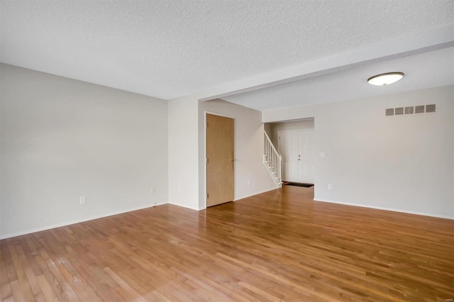 unfurnished room with a textured ceiling, hardwood / wood-style flooring, and beamed ceiling