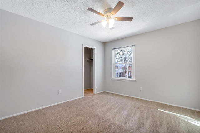 unfurnished bedroom featuring a textured ceiling, ceiling fan, a spacious closet, and light carpet