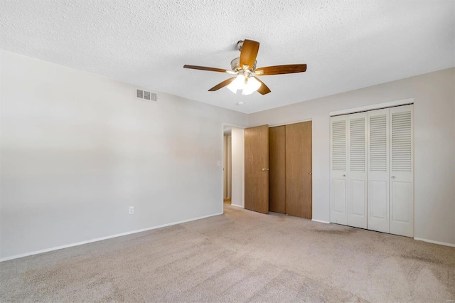 unfurnished bedroom with a textured ceiling, ceiling fan, light carpet, and multiple closets