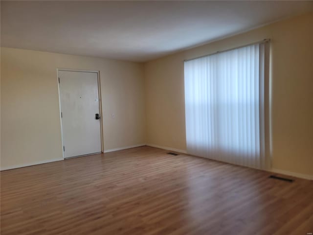 empty room featuring wood finished floors, visible vents, and baseboards