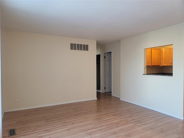 spare room featuring light wood finished floors, visible vents, and baseboards