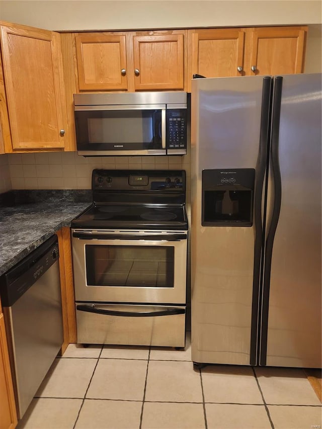 kitchen with appliances with stainless steel finishes, dark stone countertops, light tile patterned flooring, and decorative backsplash