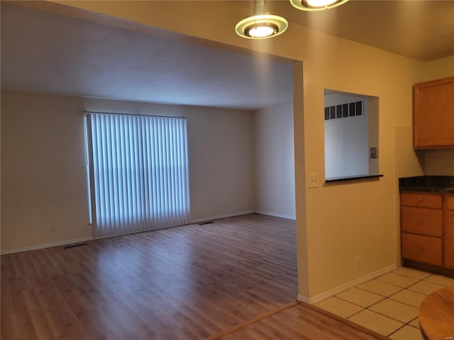 kitchen with light wood-type flooring, dark countertops, brown cabinets, and visible vents