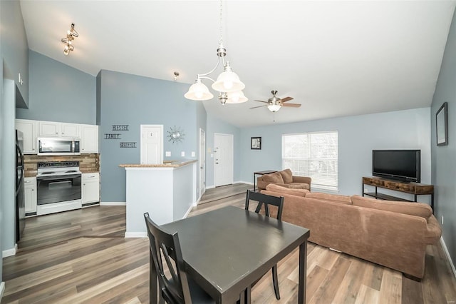 dining space featuring ceiling fan with notable chandelier, lofted ceiling, wood finished floors, and baseboards