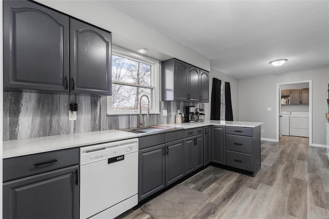 kitchen with washer and clothes dryer, white dishwasher, kitchen peninsula, sink, and wood-type flooring