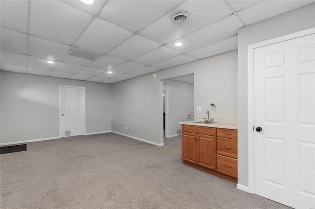 basement with a paneled ceiling, sink, and light colored carpet