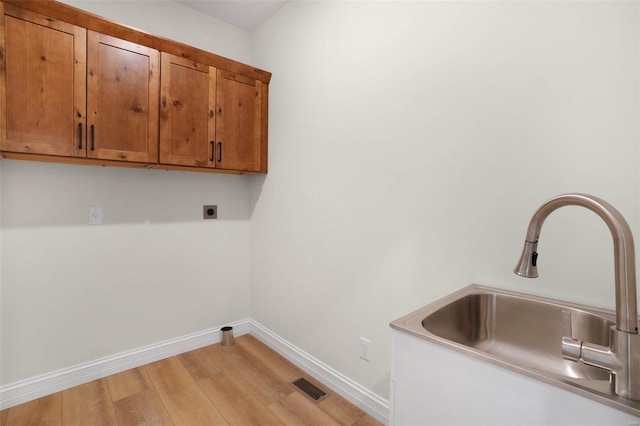 clothes washing area with hookup for an electric dryer, cabinets, light wood-type flooring, and sink