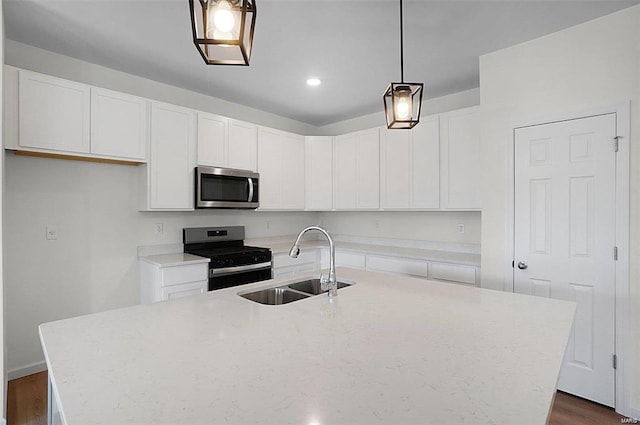 kitchen with an island with sink, white cabinetry, sink, hanging light fixtures, and stainless steel appliances