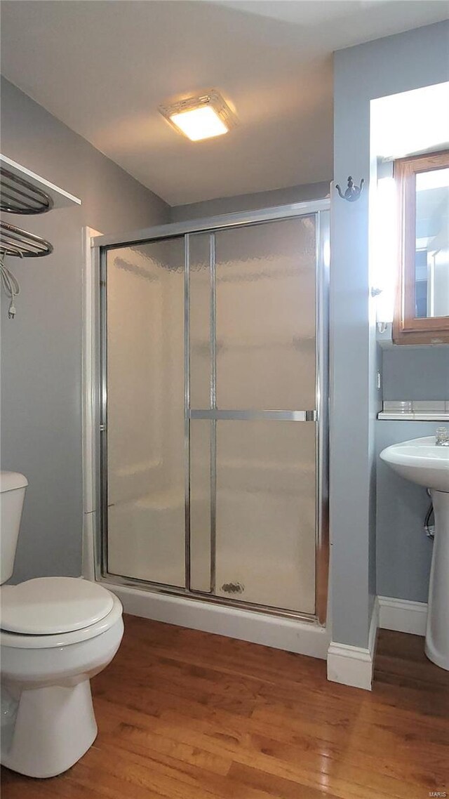 bathroom with toilet, a shower with door, and hardwood / wood-style floors