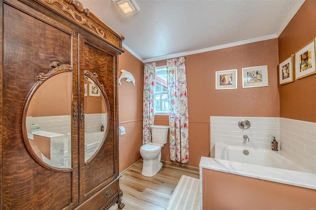 bathroom with hardwood / wood-style floors, a bathing tub, toilet, ornamental molding, and a textured ceiling