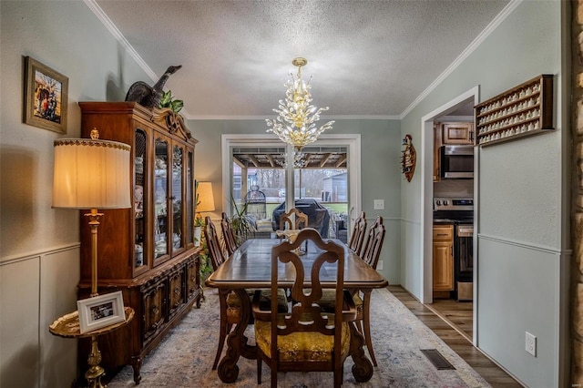 dining area featuring a chandelier, wood-type flooring, a textured ceiling, and ornamental molding