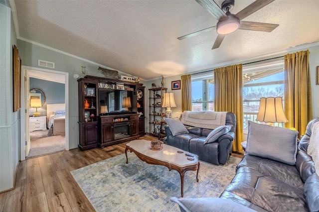 living room featuring light wood-type flooring, ornamental molding, a textured ceiling, ceiling fan, and lofted ceiling