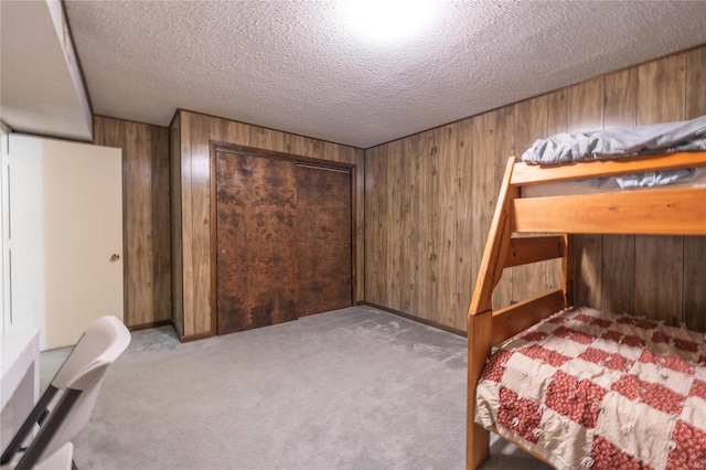 unfurnished bedroom featuring a textured ceiling, light colored carpet, a closet, and wood walls