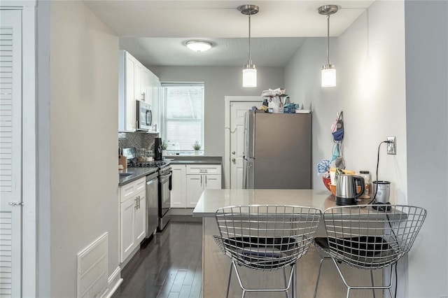 kitchen featuring kitchen peninsula, appliances with stainless steel finishes, a breakfast bar, decorative light fixtures, and white cabinets