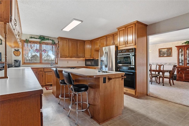 kitchen featuring a breakfast bar, a textured ceiling, sink, black appliances, and a center island