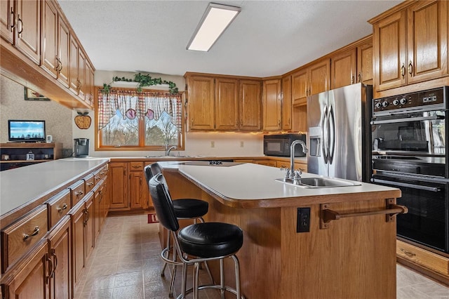 kitchen with a kitchen bar, a center island with sink, black appliances, and sink