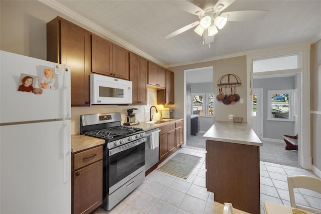 kitchen with appliances with stainless steel finishes, sink, ornamental molding, light tile patterned floors, and ceiling fan