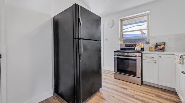 kitchen featuring white cabinetry, black fridge, light hardwood / wood-style flooring, and stainless steel range with gas stovetop