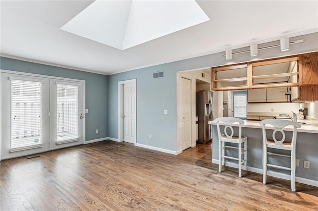 kitchen with hardwood / wood-style floors, stainless steel refrigerator with ice dispenser, a skylight, a kitchen bar, and kitchen peninsula