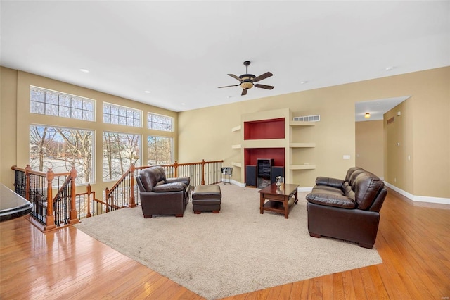 living room with built in features, ceiling fan, baseboards, and wood-type flooring