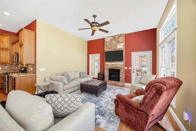 living area with light wood-style flooring, a fireplace, baseboards, and ceiling fan