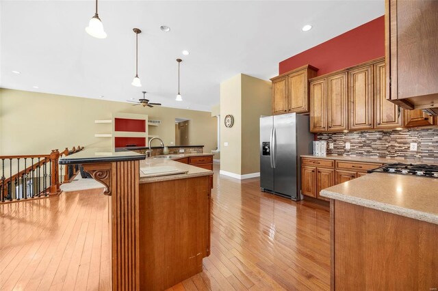 kitchen with brown cabinets, a sink, tasteful backsplash, stainless steel fridge, and light wood finished floors