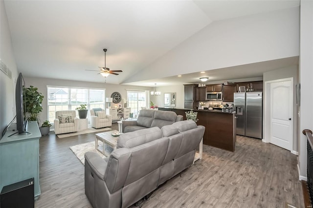 living room featuring high vaulted ceiling, ceiling fan with notable chandelier, and light wood-type flooring