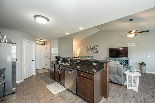 kitchen with lofted ceiling, sink, dark brown cabinets, dark stone countertops, and appliances with stainless steel finishes