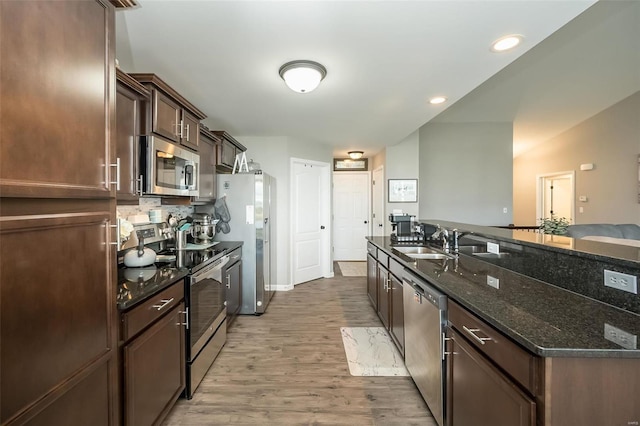 kitchen with dark brown cabinetry, sink, dark stone countertops, appliances with stainless steel finishes, and light hardwood / wood-style floors