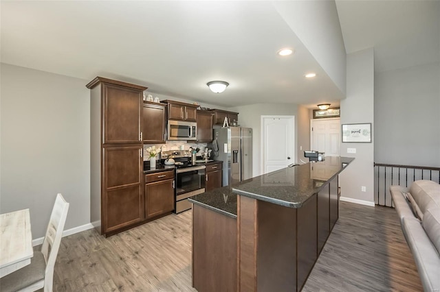 kitchen featuring dark brown cabinetry, light wood-type flooring, dark stone countertops, stainless steel appliances, and backsplash