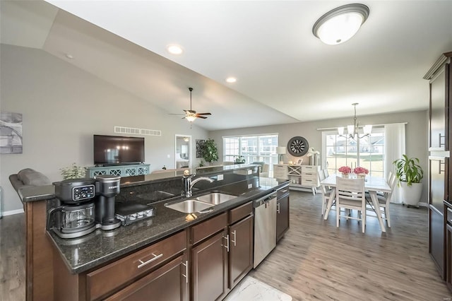 kitchen featuring lofted ceiling, sink, decorative light fixtures, dark stone countertops, and stainless steel dishwasher