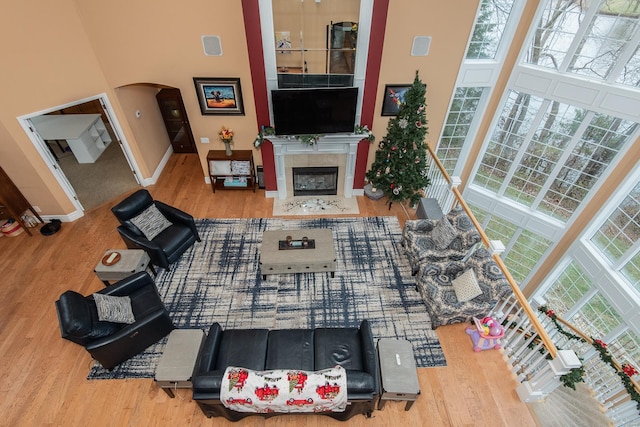 living room with wood-type flooring, a towering ceiling, and a tiled fireplace