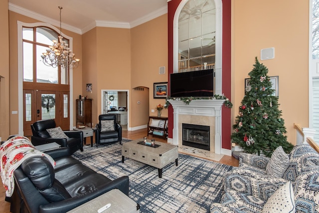 living room with a towering ceiling, ornamental molding, hardwood / wood-style flooring, an inviting chandelier, and a fireplace