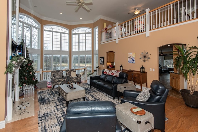 living room with ceiling fan, light hardwood / wood-style floors, ornamental molding, and a high ceiling