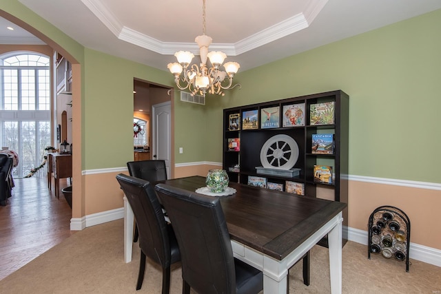 carpeted dining room featuring a tray ceiling, crown molding, and a notable chandelier