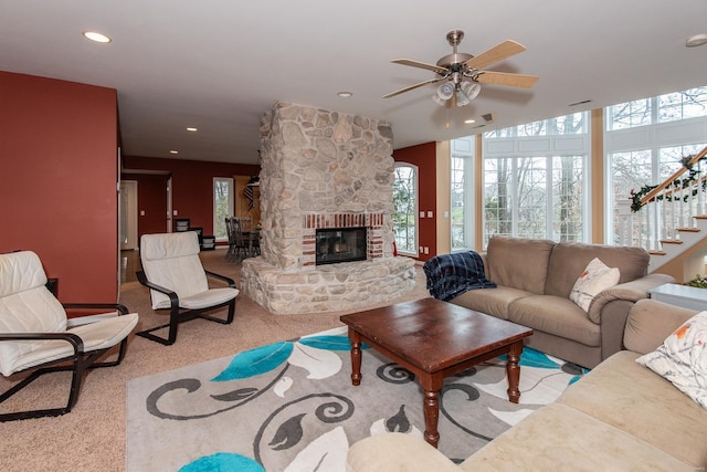 carpeted living room with a stone fireplace and ceiling fan