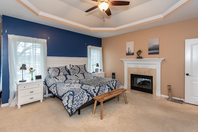 carpeted bedroom with ceiling fan, a raised ceiling, and a tile fireplace