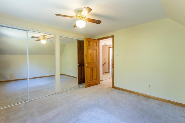 unfurnished bedroom with two closets, ceiling fan, lofted ceiling, and light colored carpet