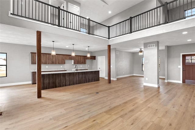 living room with sink, a towering ceiling, light hardwood / wood-style floors, and ceiling fan