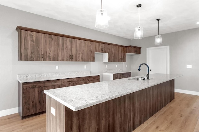 kitchen featuring sink, hanging light fixtures, light hardwood / wood-style floors, light stone countertops, and a center island with sink