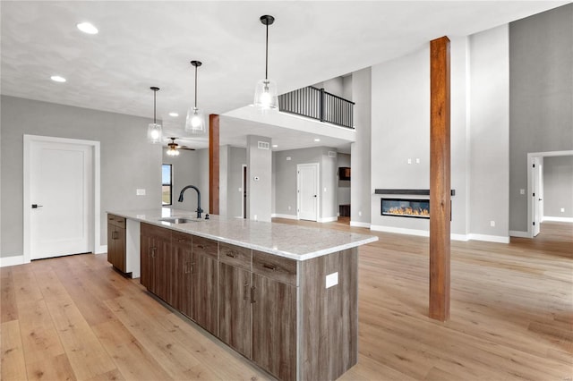 kitchen featuring light stone counters, ceiling fan, sink, and a center island with sink