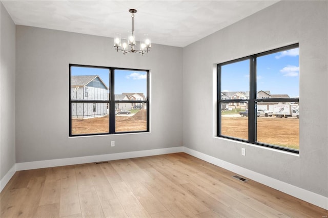 spare room with a notable chandelier and light hardwood / wood-style flooring